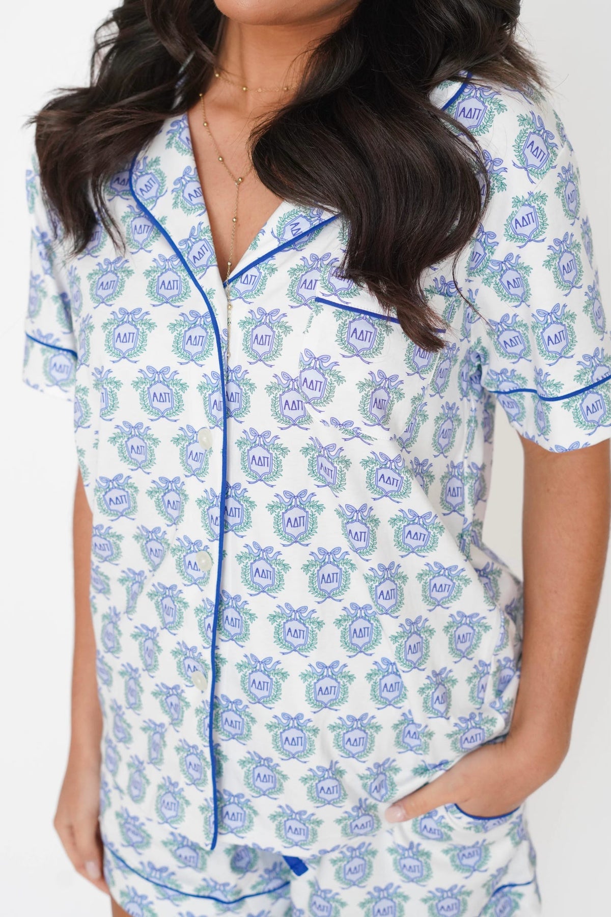 A close-up of a woman wearing a short-sleeve pajama top with a white base, blue and green monogram pattern, and blue piping trim.