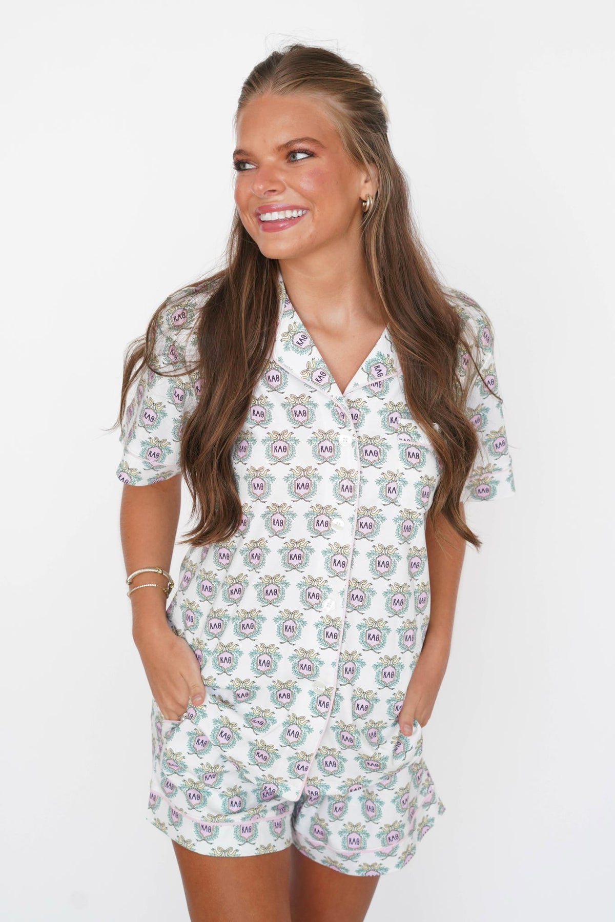 A woman modeling a short-sleeve button-front romper with an allover paisley print on a white background, photographed against a plain white studio backdrop.