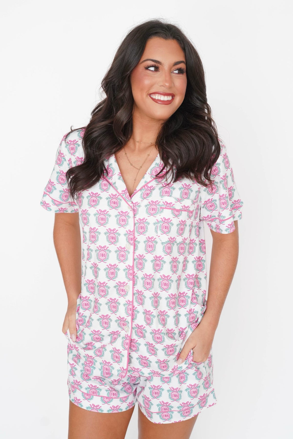A woman modeling a short-sleeve button-front pajama set with matching shorts, featuring a white base with a pink and gray floral pattern, against a plain white background.