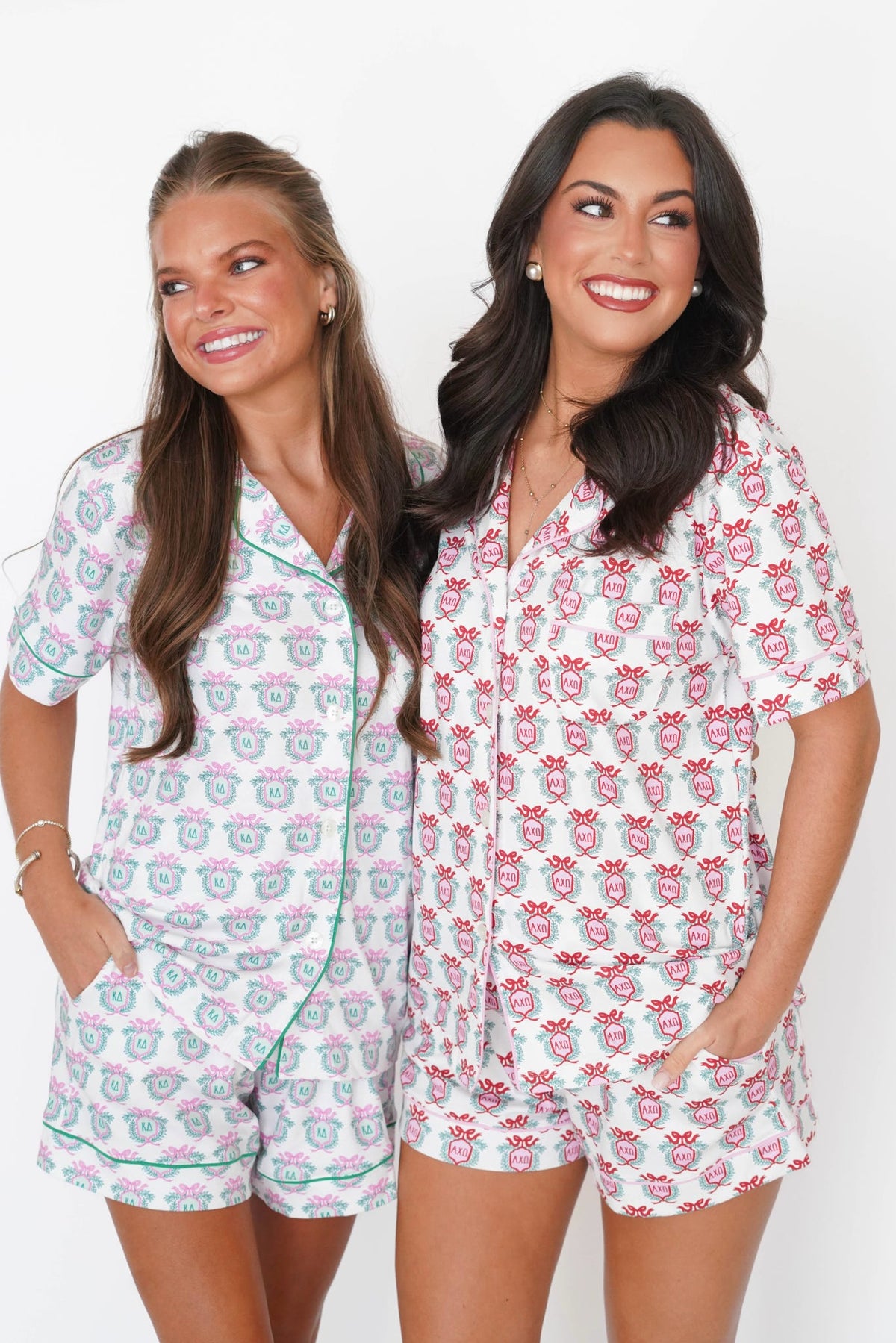 Two women modeling matching short-sleeve pajama sets with a white base and pink floral print, standing against a plain white background.