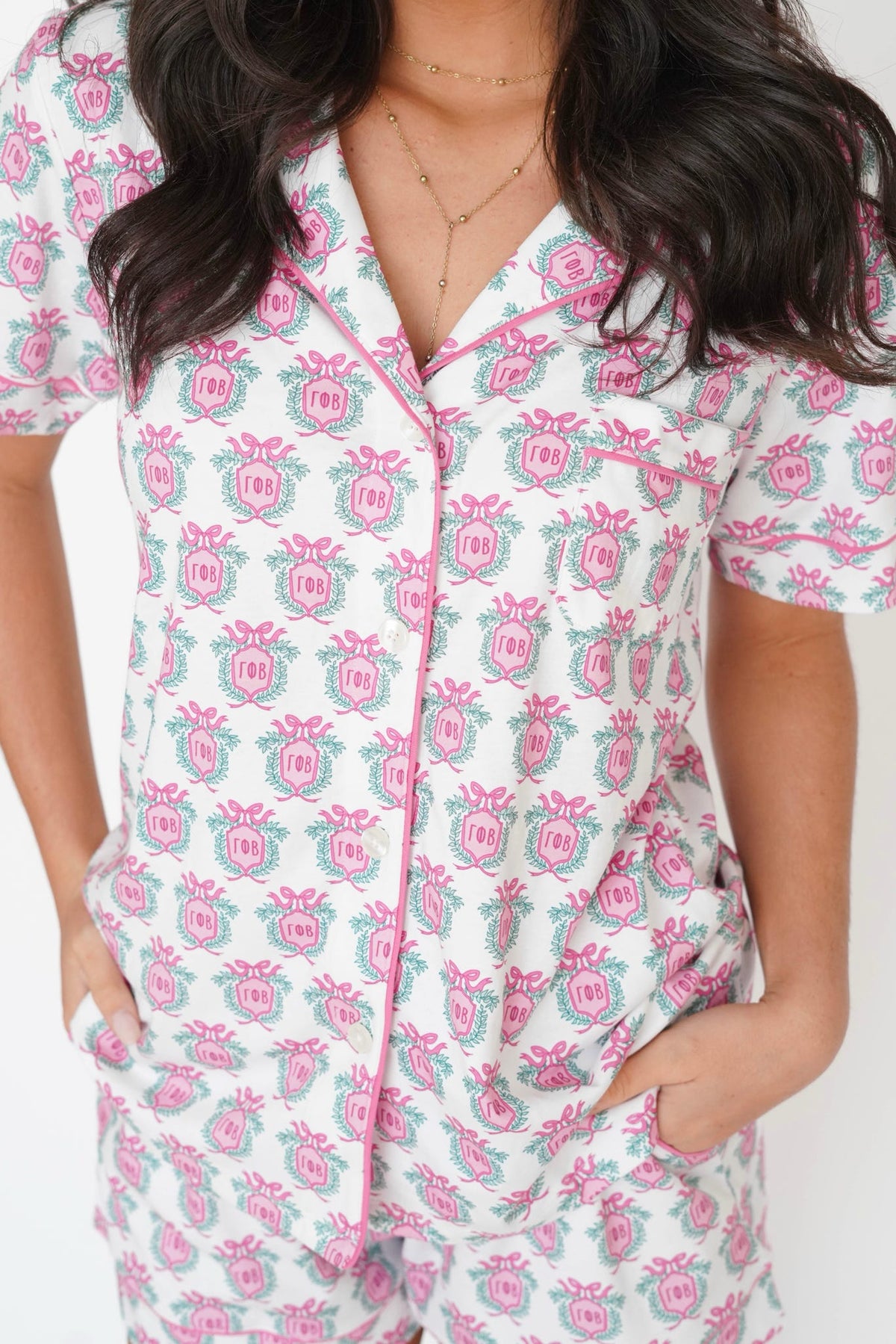 A close-up of a person wearing a short-sleeve pajama top with a white base and an allover pink and teal floral crest pattern, paired with matching shorts.