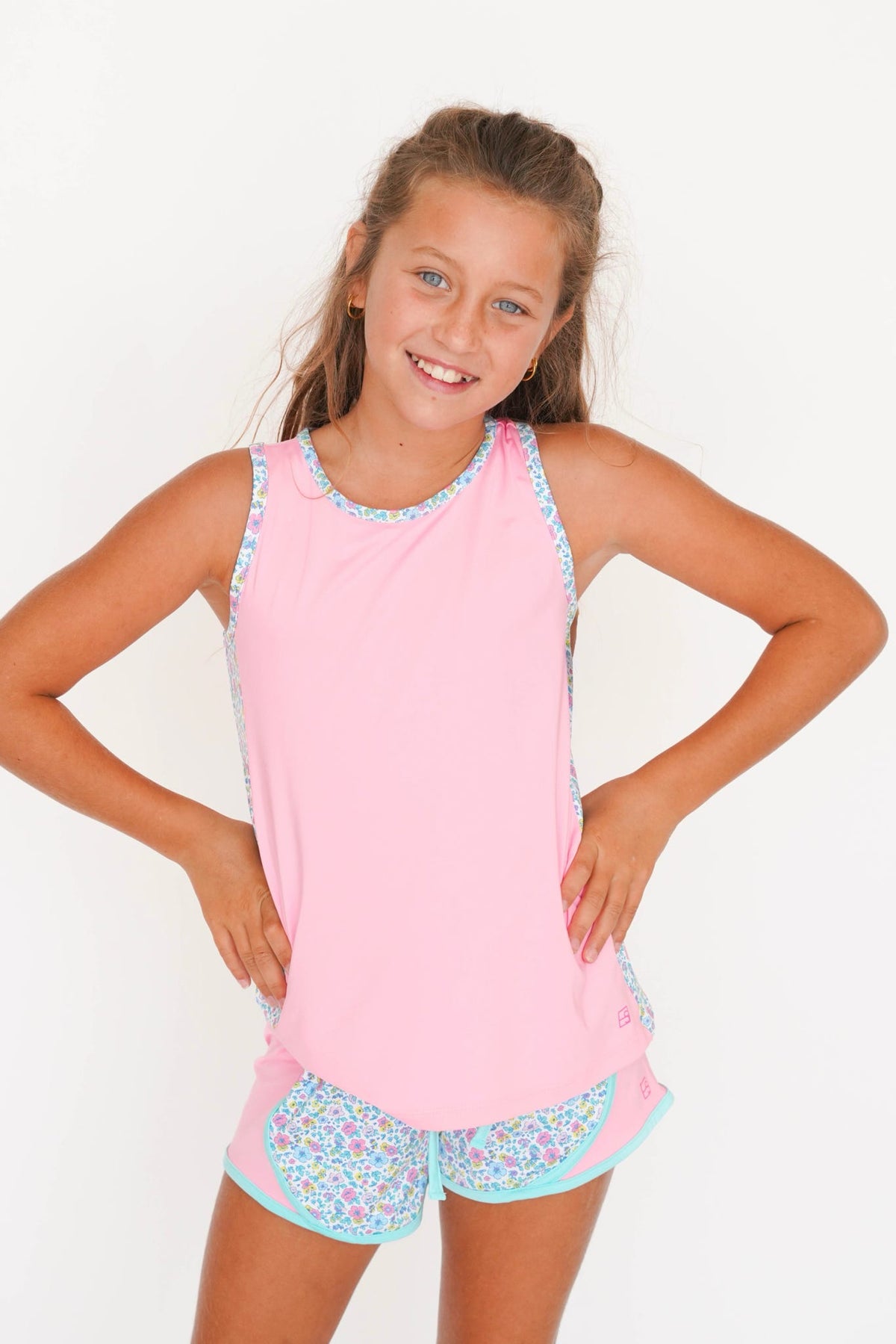 A young girl smiling and posing in a light pink sleeveless tank top and matching light blue patterned athletic shorts against a plain white background.
