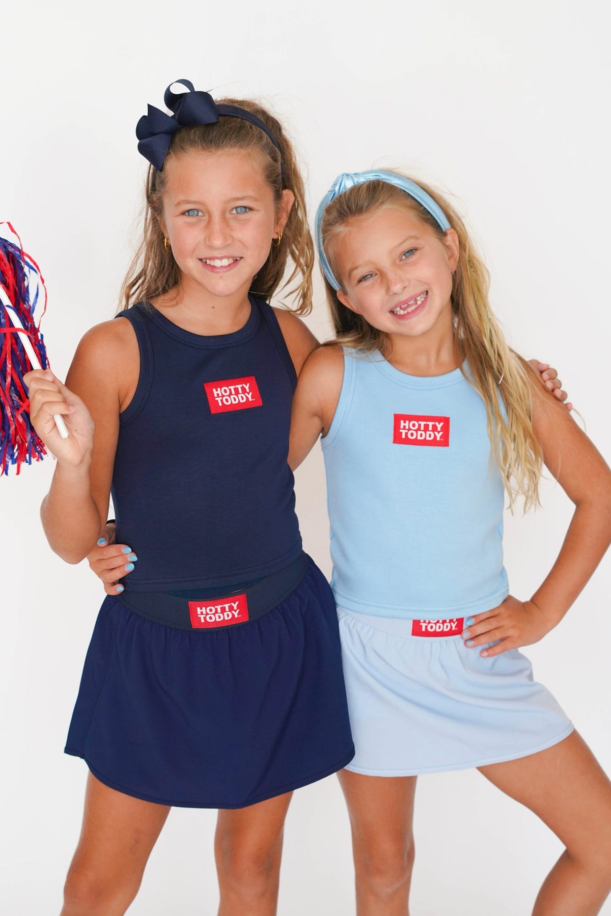Two young girls modeling matching sleeveless athletic outfits with red 'HOTTY TODAY!' patches on the chest, posed against a plain white studio background.