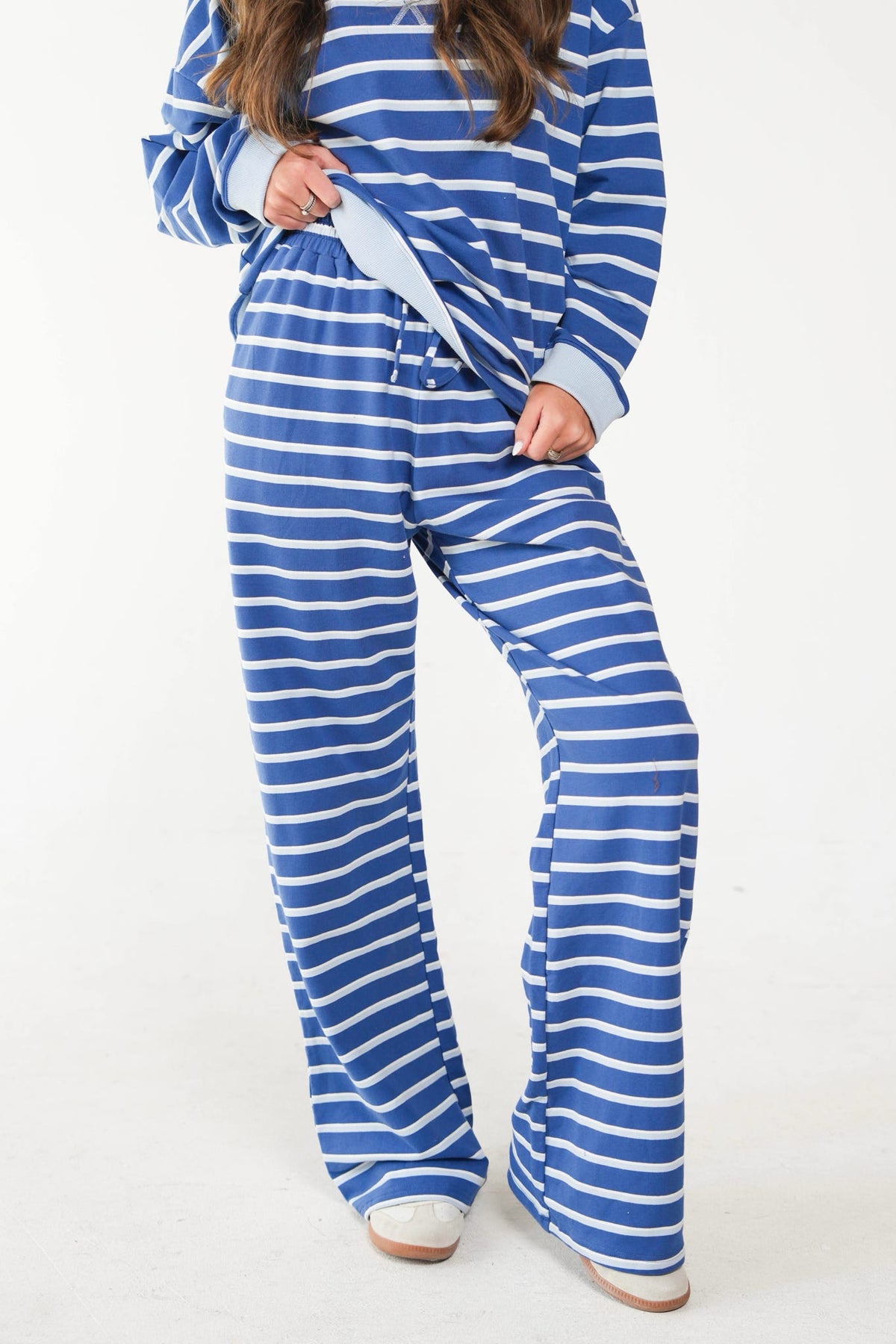 A person wearing a matching blue and white striped lounge set with a long-sleeve top and wide-leg pants, photographed against a plain light background.