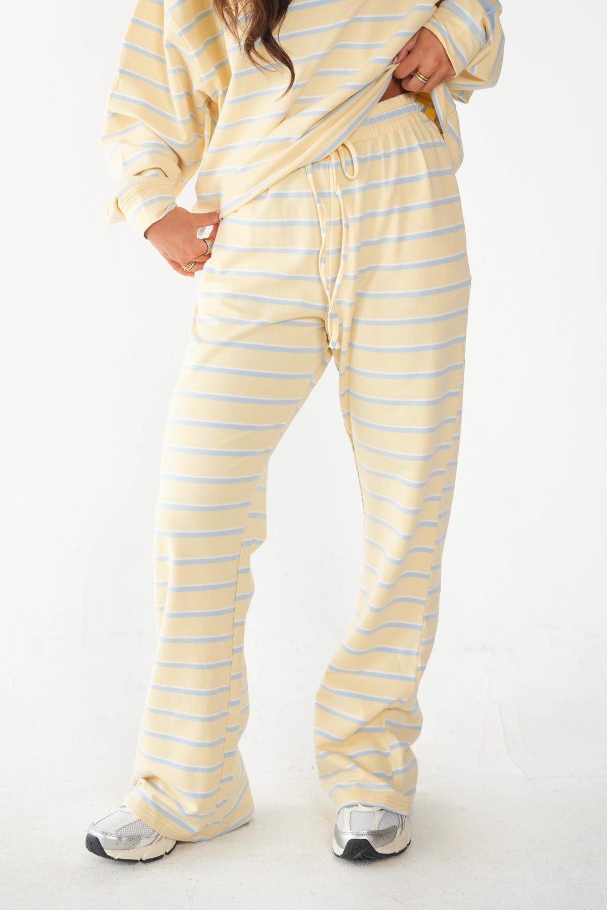 A person wearing a matching pale yellow and white striped lounge set, including a long-sleeve top and wide-leg pants, standing against a plain white studio background.