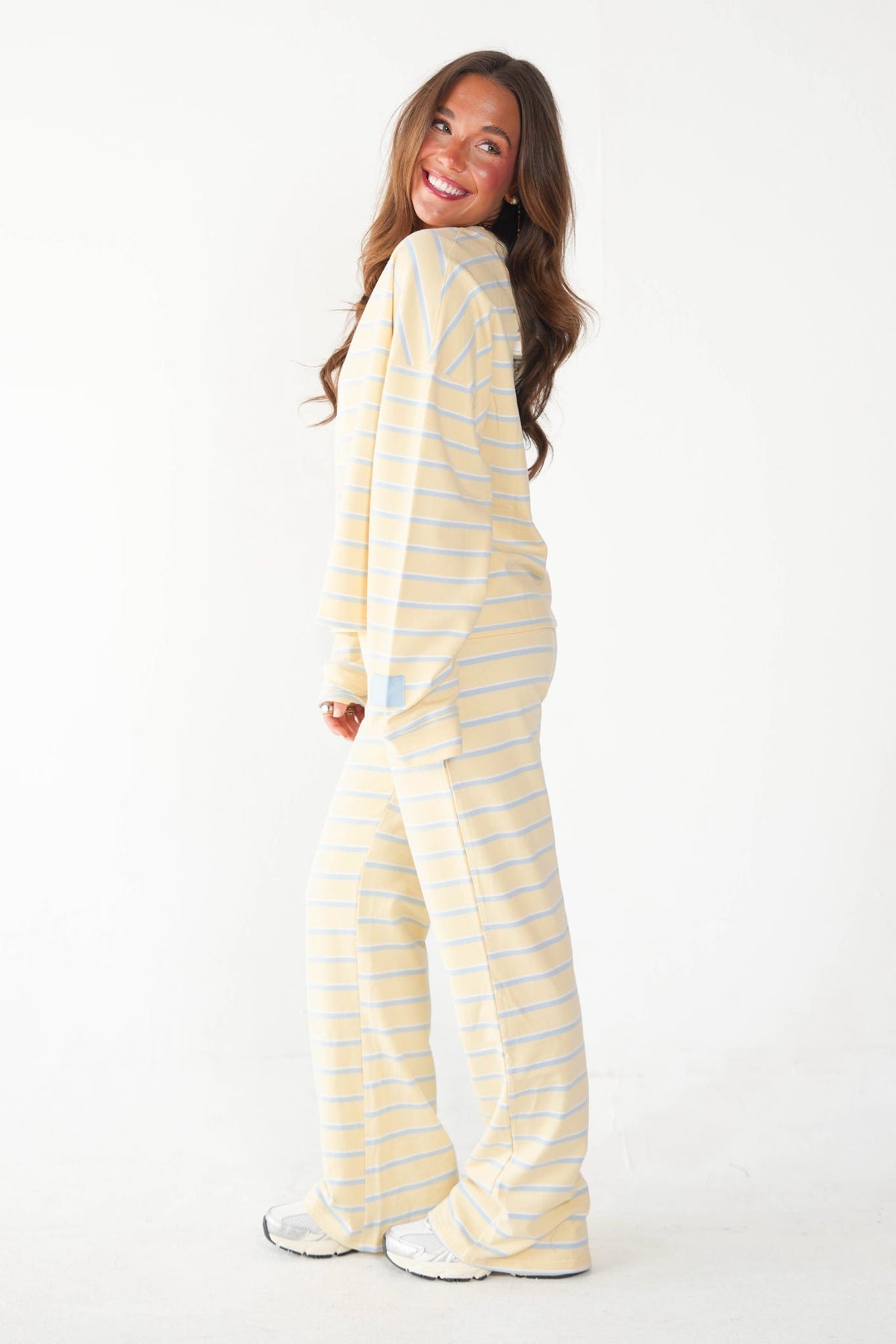 A woman modeling a matching two-piece pajama set with light yellow and white horizontal stripes, photographed against a plain white studio background.