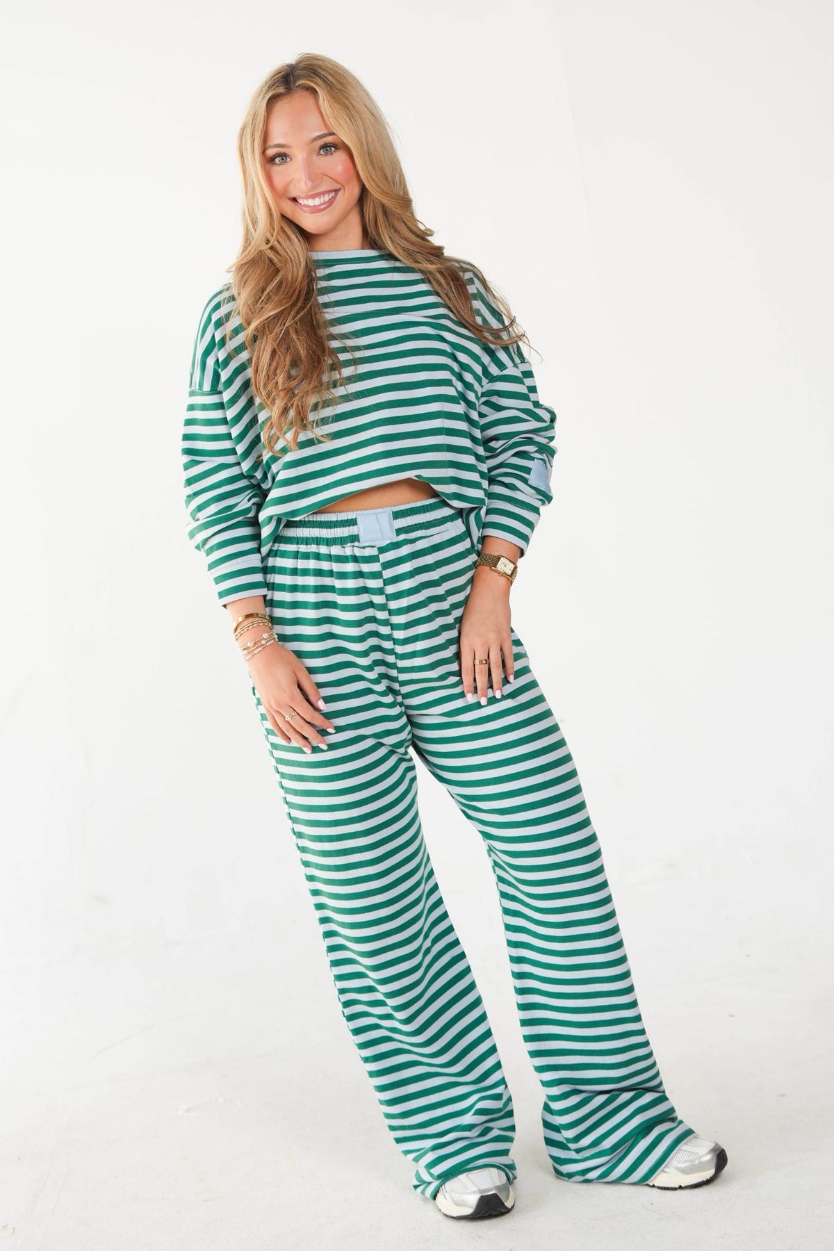 A woman modeling a matching green and white striped lounge set, featuring a cropped long-sleeve top and wide-leg pants, against a plain white studio background.