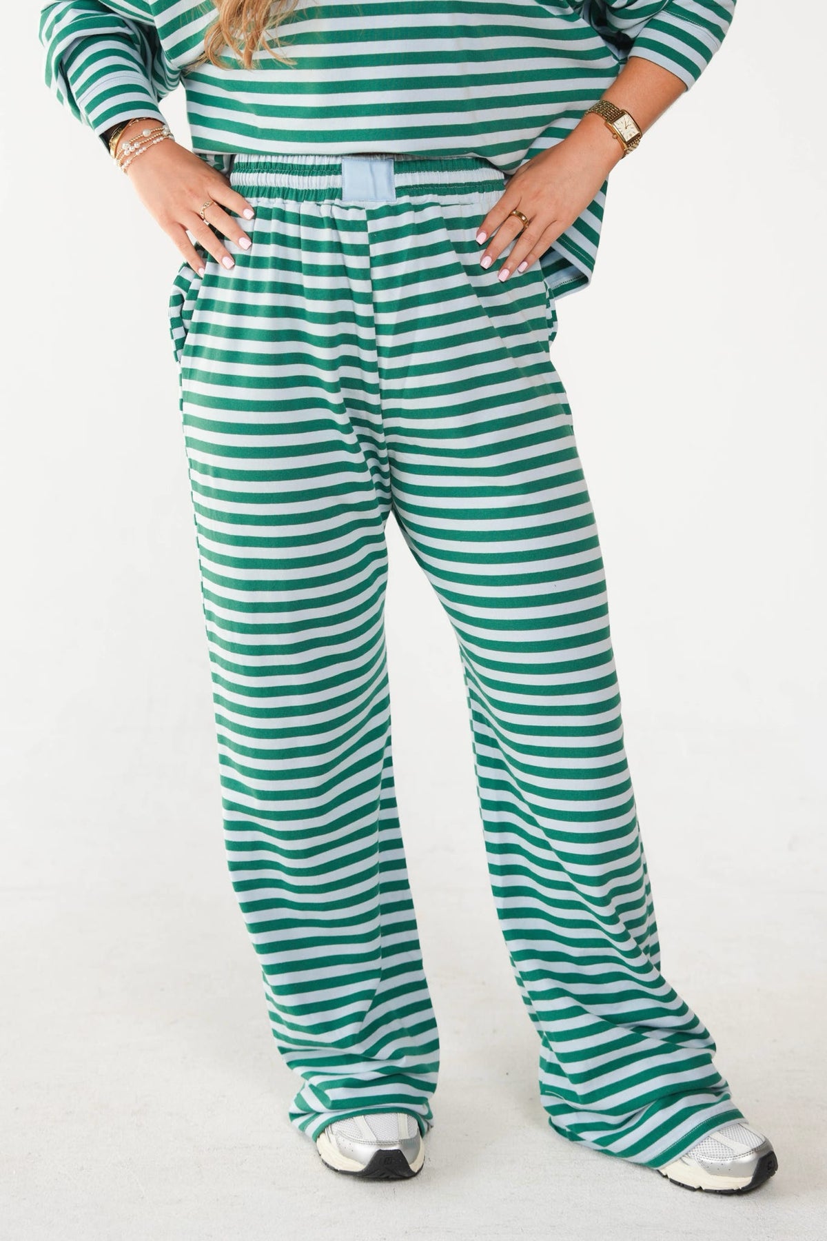 A person wearing green and white horizontally striped lounge pants with a matching striped long-sleeve top, standing against a plain light background.