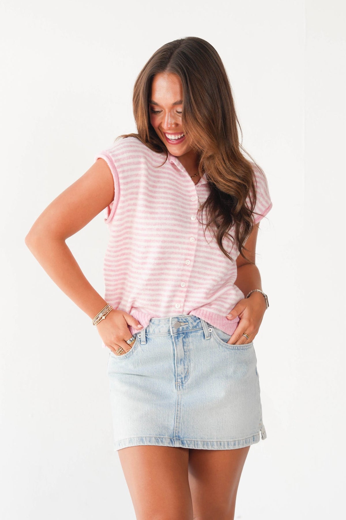 A woman modeling a light pink and white striped short-sleeve button-front top paired with a light-wash denim mini skirt, set against a plain white studio background.