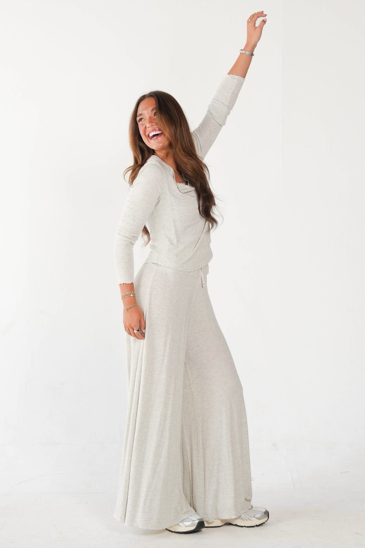 A woman modeling a light beige knit two-piece set consisting of a long-sleeve top and matching wide-leg pants, set against a plain white studio background.