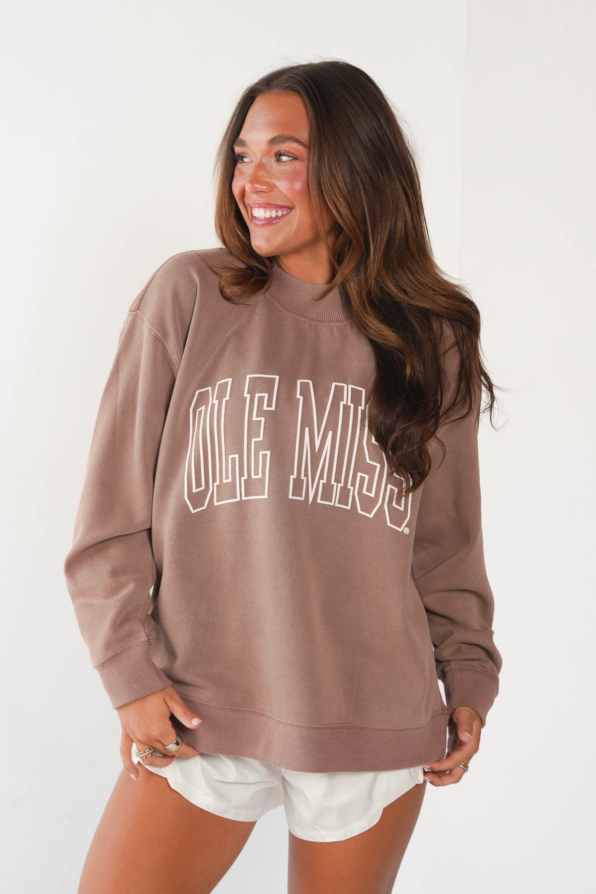 Brunette woman modeling a brown sweatshirt with white lettering and white shorts