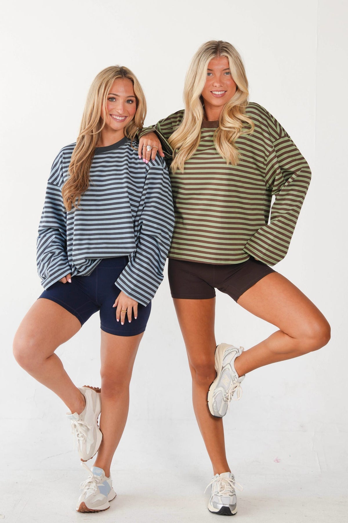 Two women posing together in matching striped long-sleeve crewneck sweatshirts and athletic shorts against a plain white studio background.