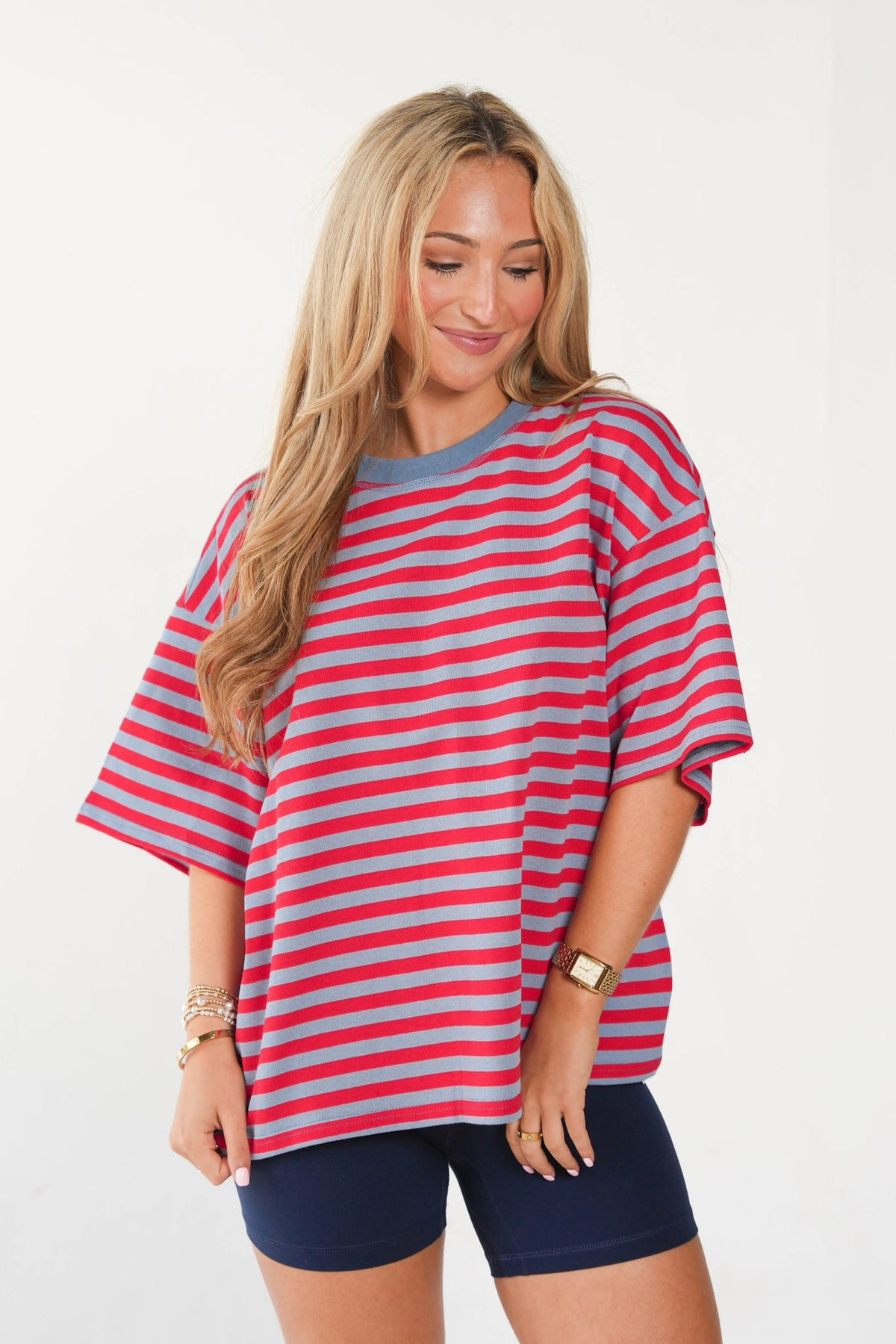 A woman wearing an oversized short-sleeve t-shirt with horizontal red and light blue stripes, paired with navy blue shorts, against a plain white background.