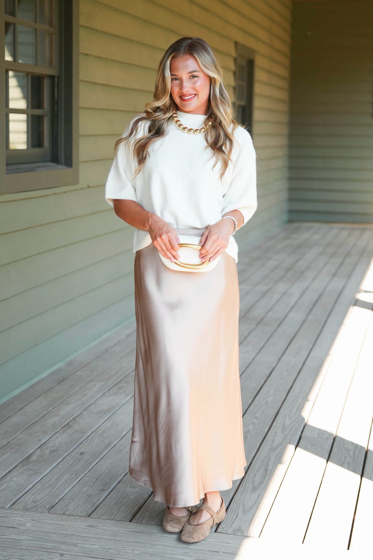 a women modeling a white sweater and taupe satin skirt