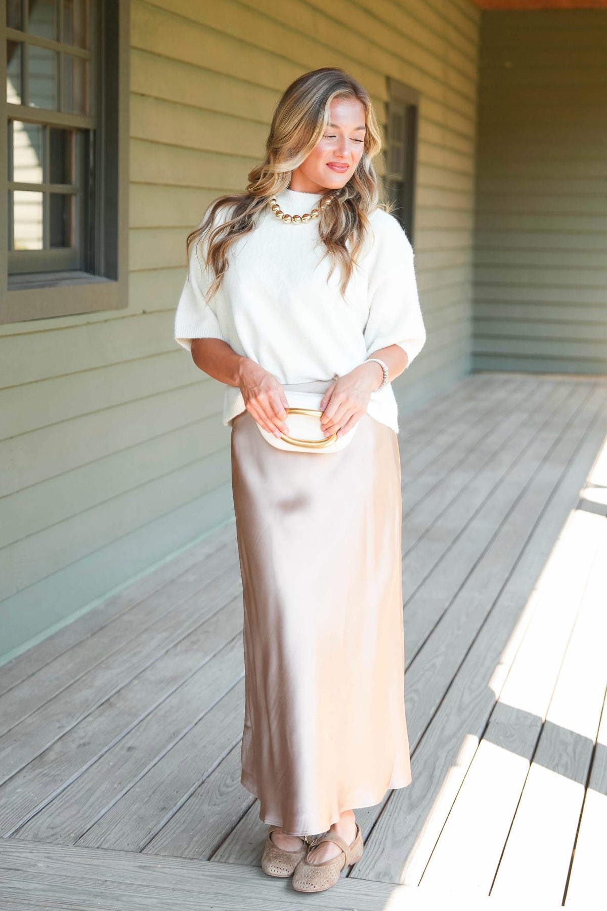 a women modeling a white sweater and taupe satin skirt