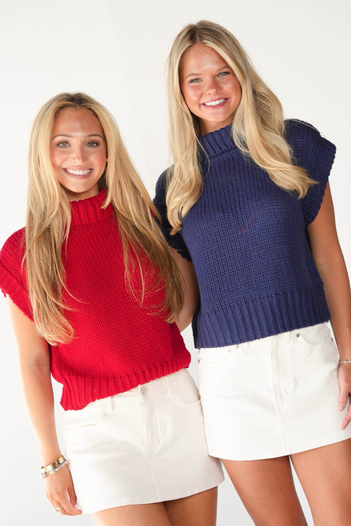 Two women modeling ribbed knit mock-neck short-sleeve tops, one in red and one in navy blue, paired with white shorts against a plain white background.