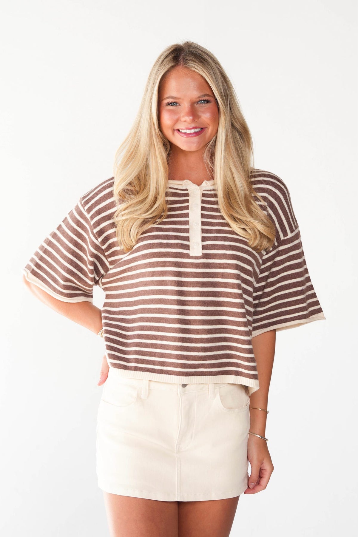 A woman modeling a brown and cream striped short-sleeve top with a split neckline, paired with cream shorts, against a plain white background.