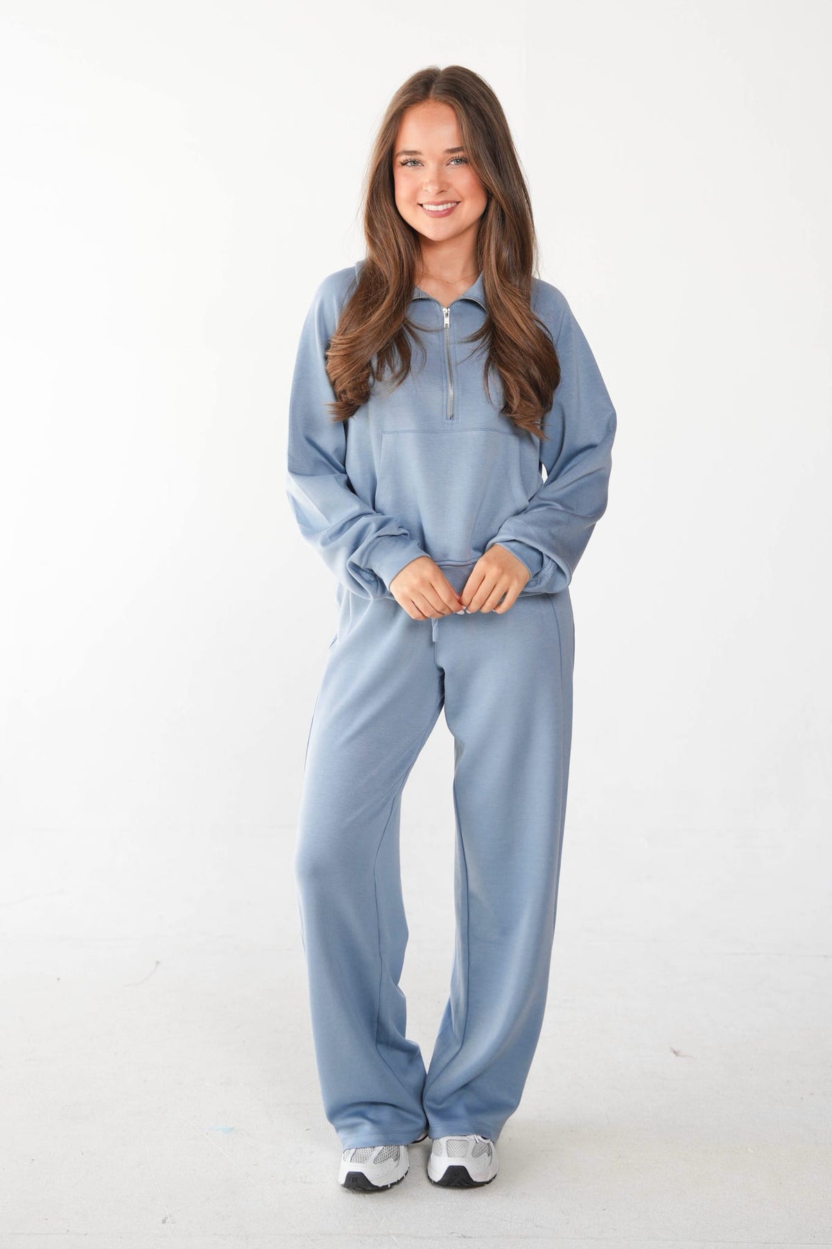 A woman modeling a light blue zip-up hoodie and matching wide-leg sweatpants against a plain white studio background.