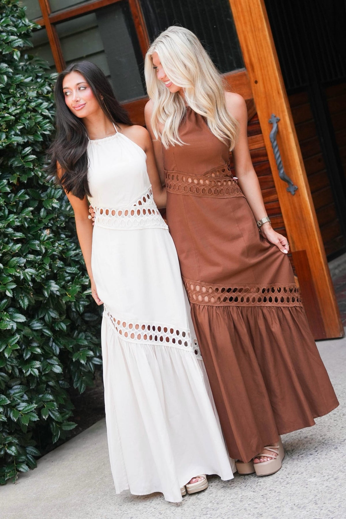 two women standing in front of a barn door modeling matching dresses. one cream dress and one brown dress