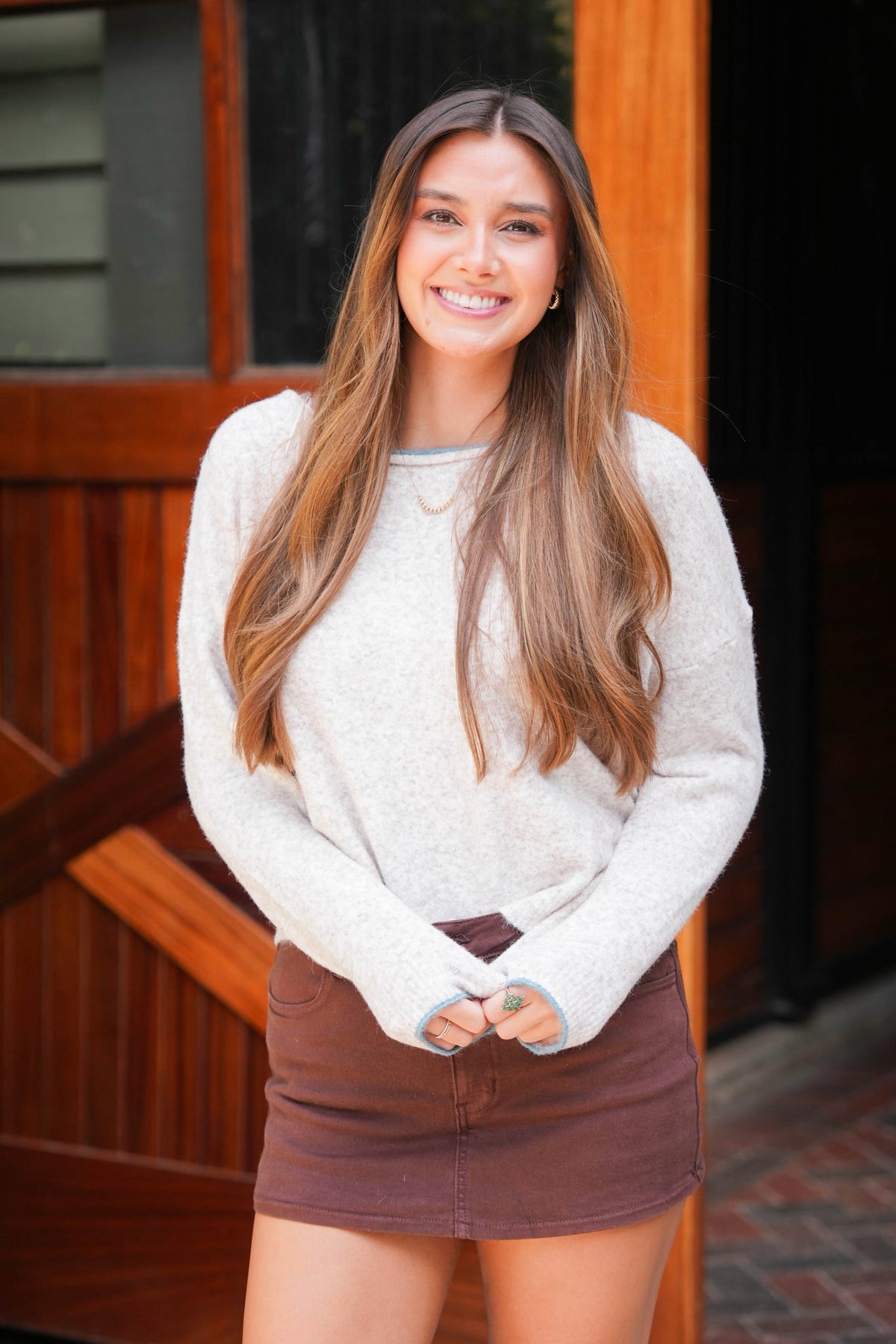 women standing in front of barn door wearing cream sweater and brown skirt