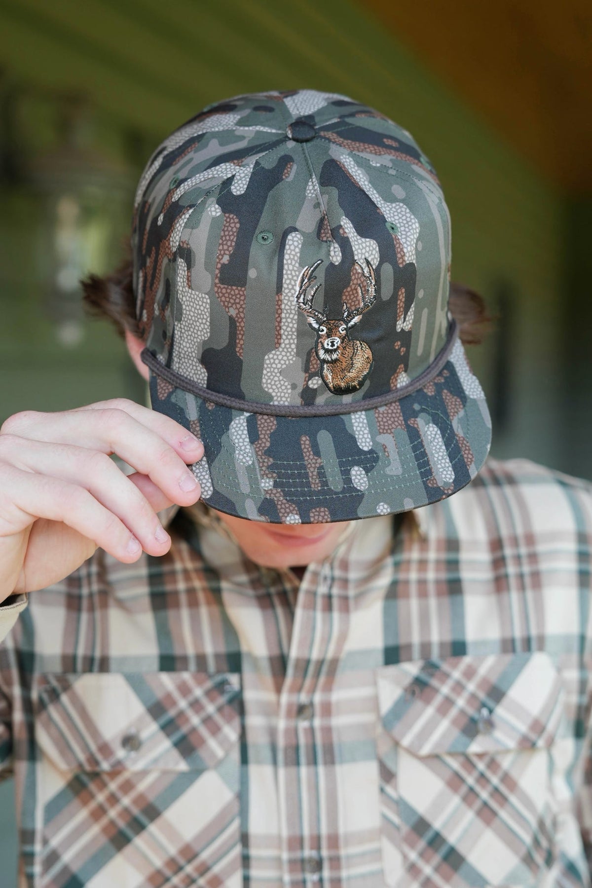 Camo hat with a deer on it and brown rope across
