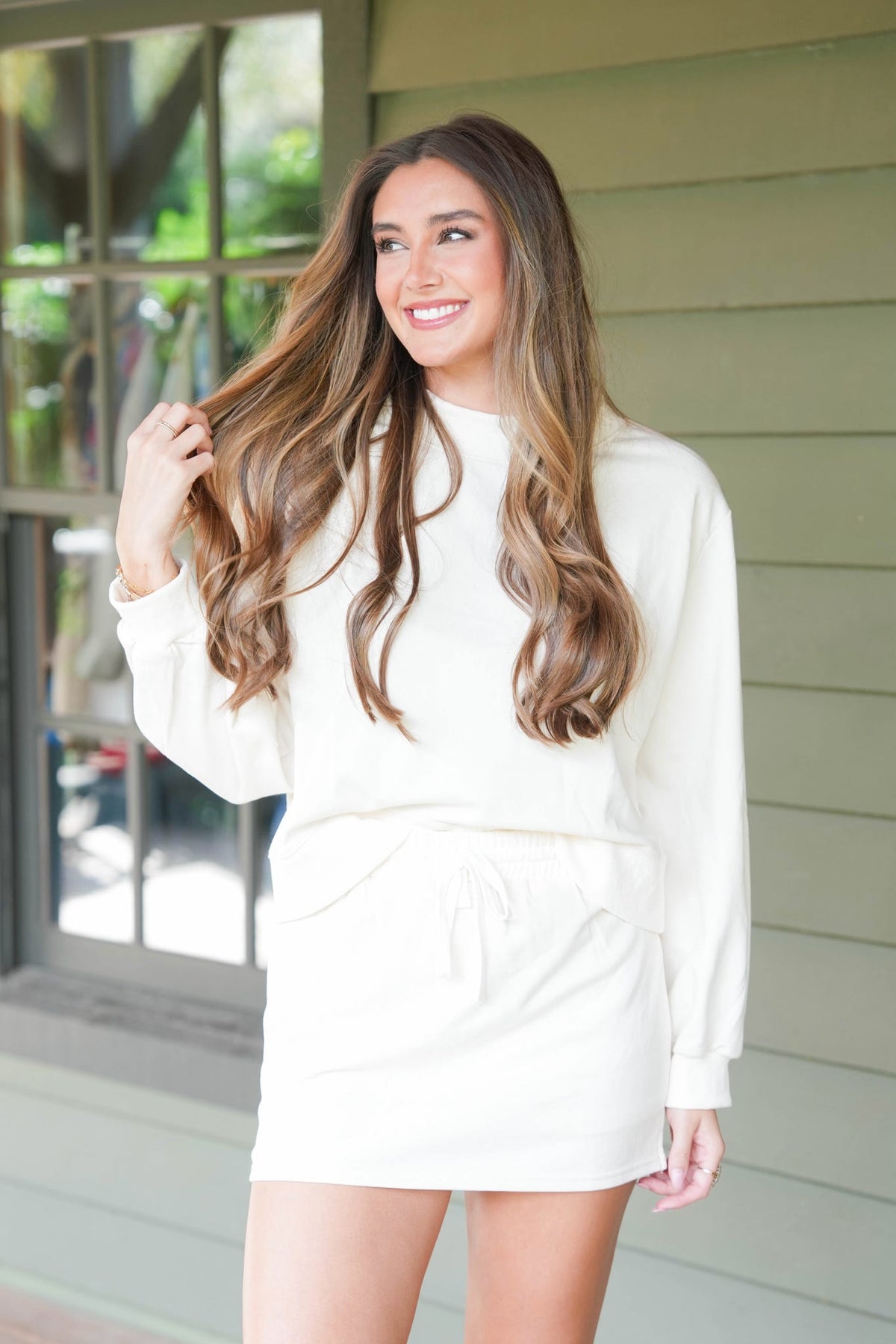 woman standing on brown deck wearing cream matching sweatshirt and skort set
