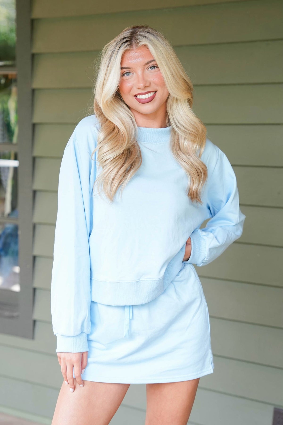 woman standing on brown deck wearing blue matching sweatshirt and skort set