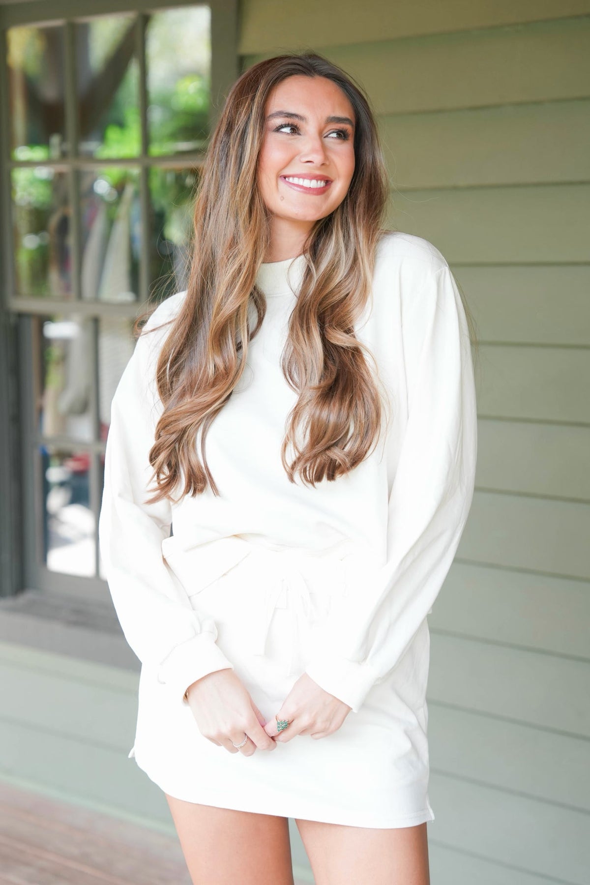 woman standing on a wooden porch wearing a cream matching sweatshirt and skort set