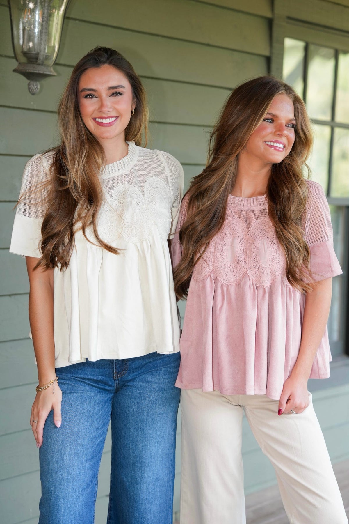 Two women modeling short-sleeve peplum tops with lace applique. The woman on the left wears an off-white top with blue jeans, and the woman on the right wears a dusty pink top with white pants.