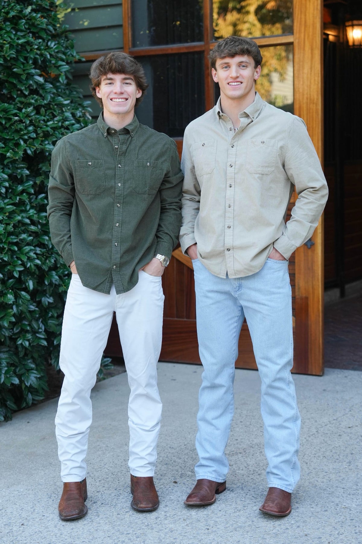 Two men standing in front of a barn door wearing green button downs with jeans and boots