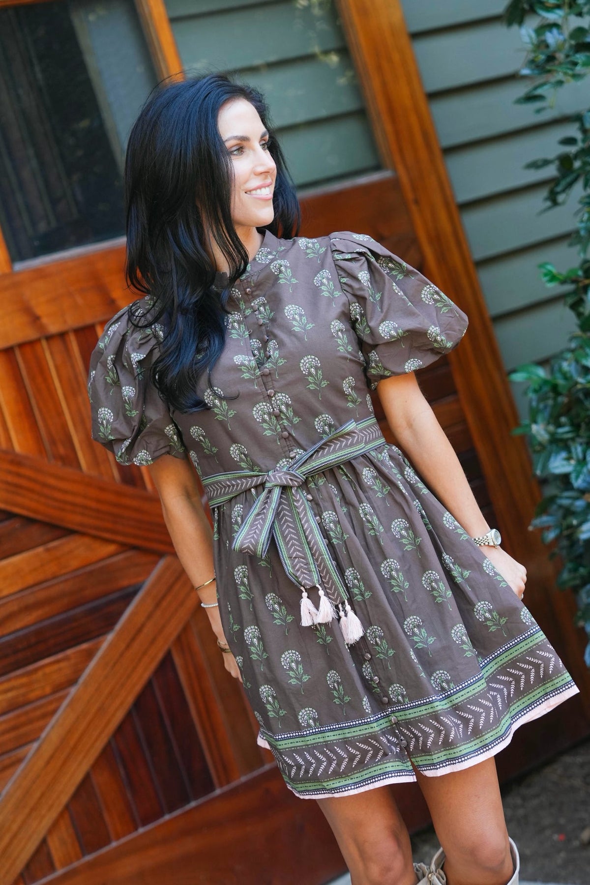 woman modeling outdoors in a brown mini dress with floral pattern and tie waist