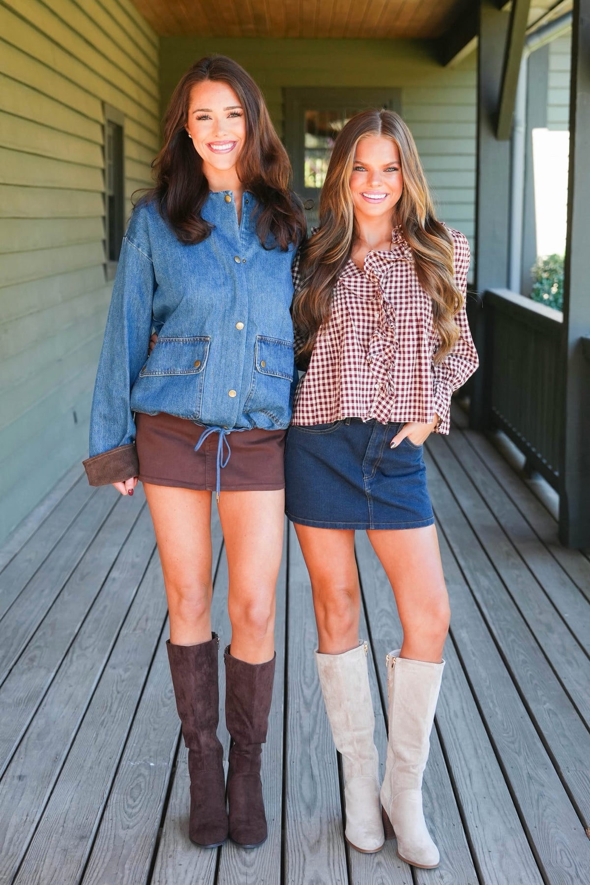 Two women standing on a wooden porch wearing casual fall fashion. The woman on the left wears a blue denim shirt, a brown mini skirt, and dark brown knee-high boots.