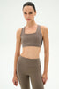 A woman modeling a matching taupe-brown activewear set consisting of a scoop-neck sports bra and high-waisted leggings, shown against a plain white studio background.