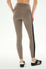 A person wearing high-waisted taupe-brown leggings with a black side stripe and beige piping, paired with black and beige sneakers, shown from the back against a white studio background.