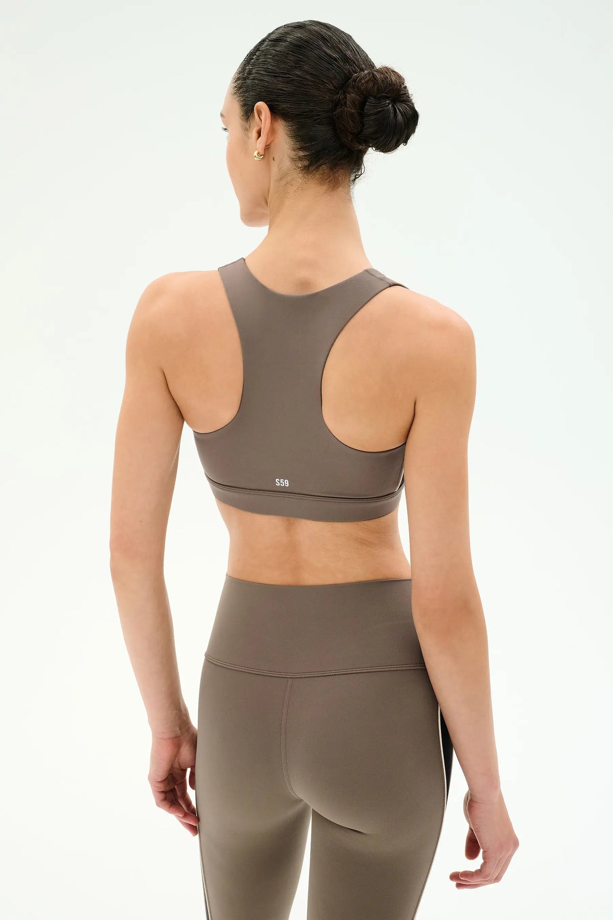 A woman shown from the back wearing a taupe brown sports bra and matching high-waisted leggings against a clean white studio background.