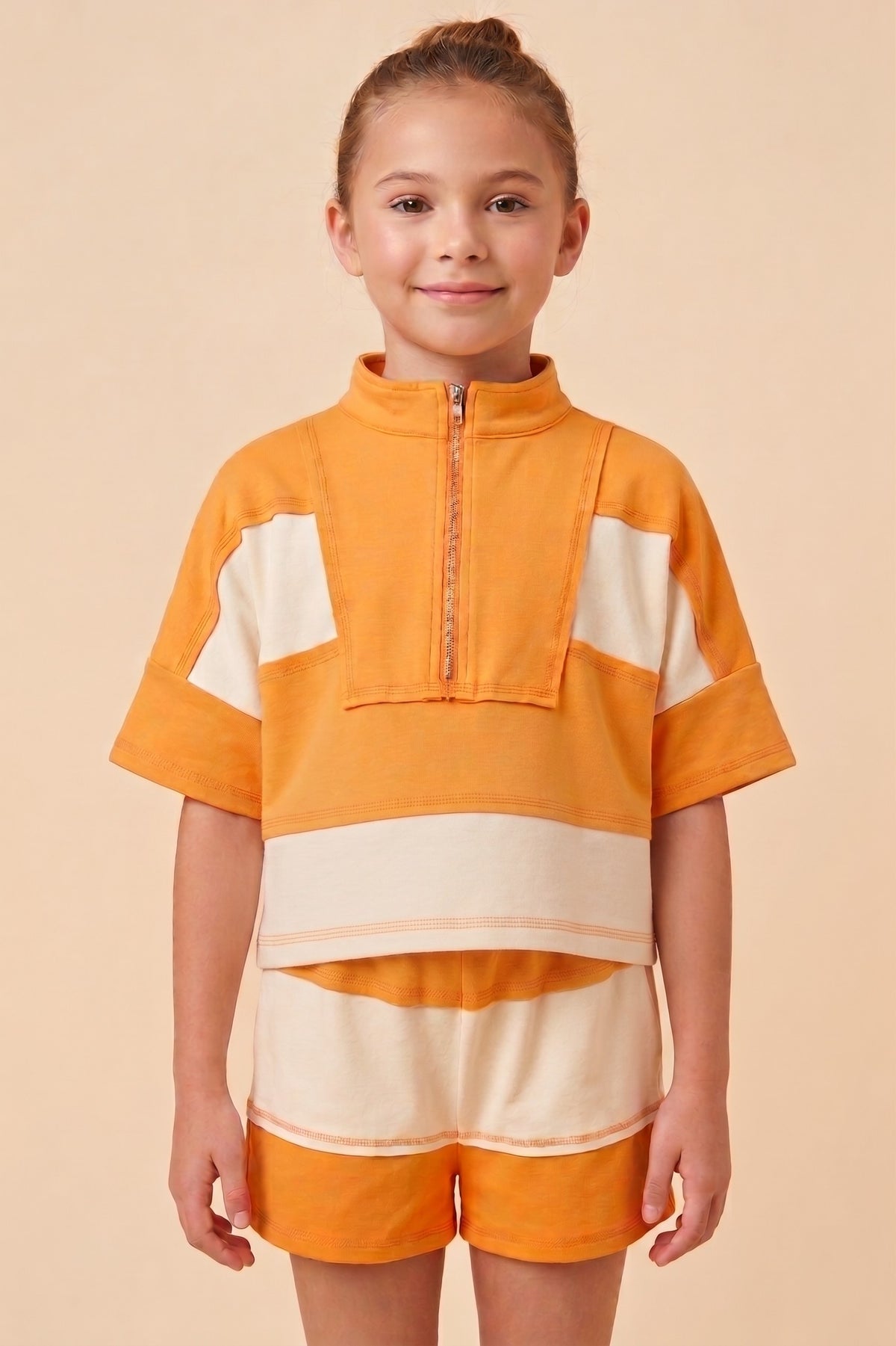 Child wearing an orange and beige outfit on a beige background