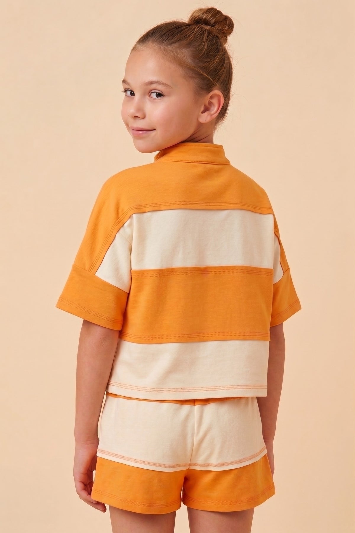 Young girl wearing an orange and beige outfit against a beige background