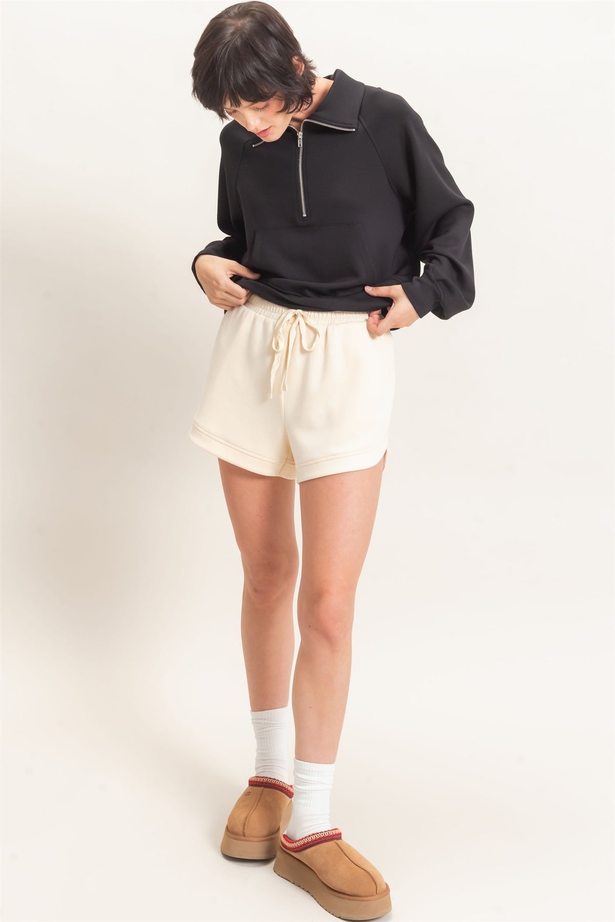 Person wearing a black sweater, cream shorts, and tan shoes on a white background