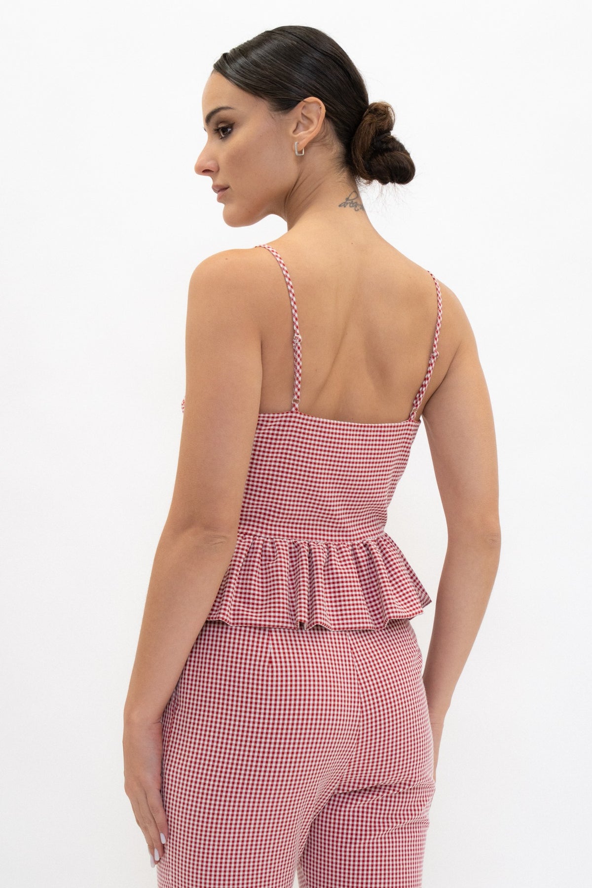 A woman shown from the back wearing a pink and white gingham romper with thin straps and a ruffled waist, against a plain white studio background.
