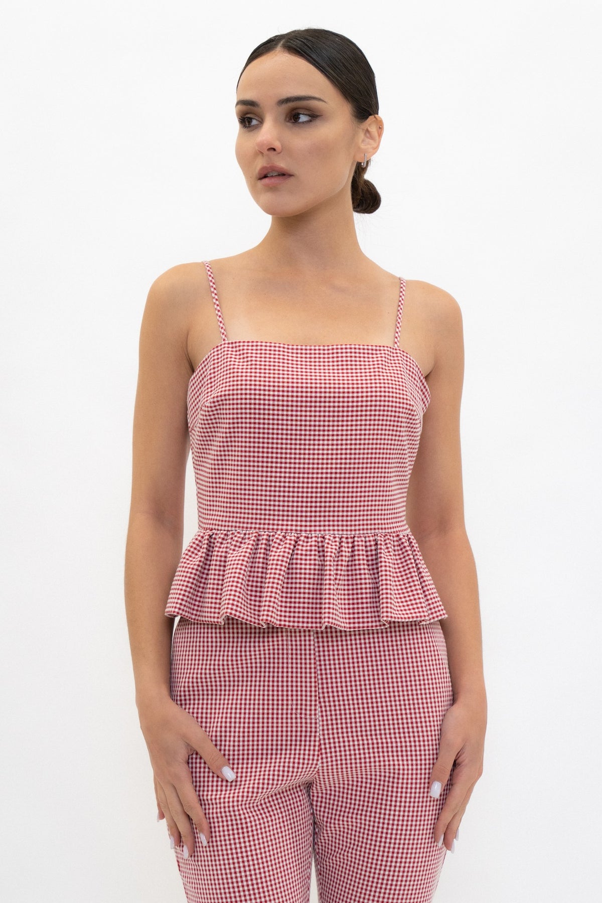 A woman modeling a matching two-piece gingham set consisting of a pink and white checkered camisole top with a peplum waist and coordinating pants, shot against a plain white background.