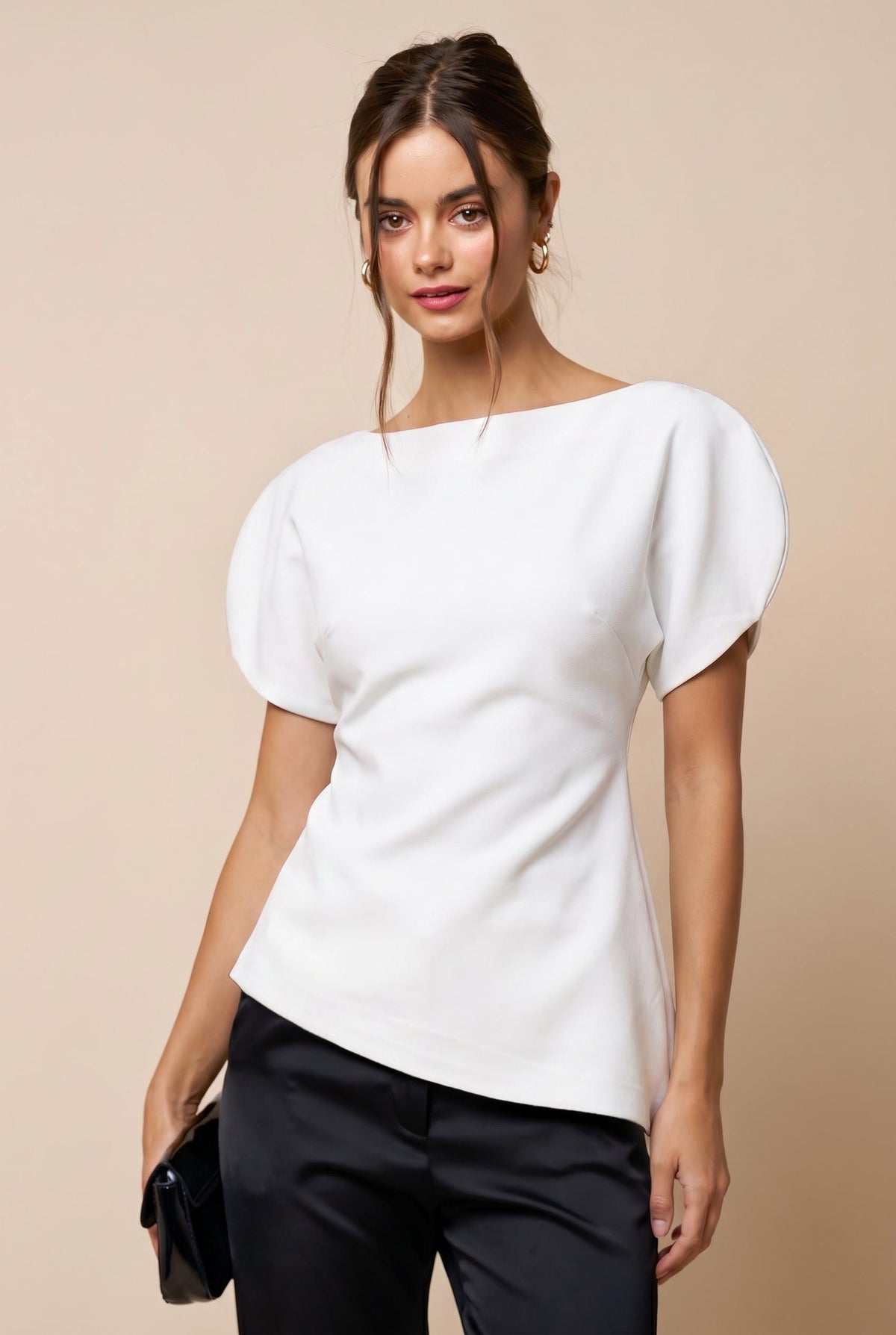 A woman modeling a white short-sleeve top with voluminous puff sleeves and a boat neckline, paired with black trousers, against a solid beige background.