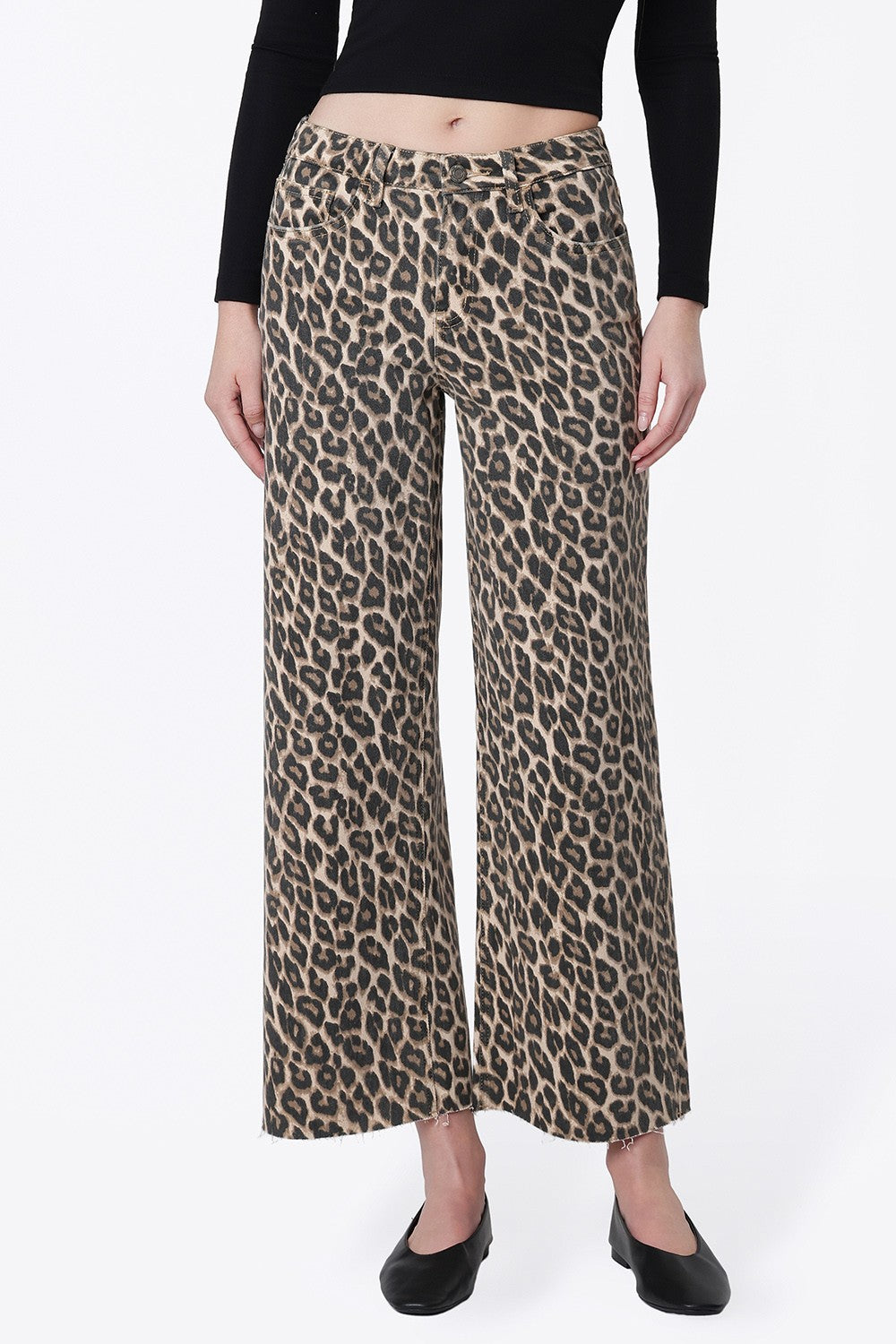 A model wearing high-waisted, wide-leg cropped pants with a beige and brown leopard print, styled with a black long-sleeve crop top and black flats against a white studio background.