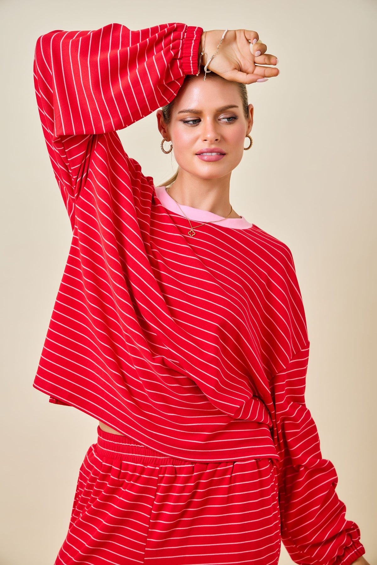 A woman modeling a red and white striped long-sleeve top and matching bottoms against a solid beige background.