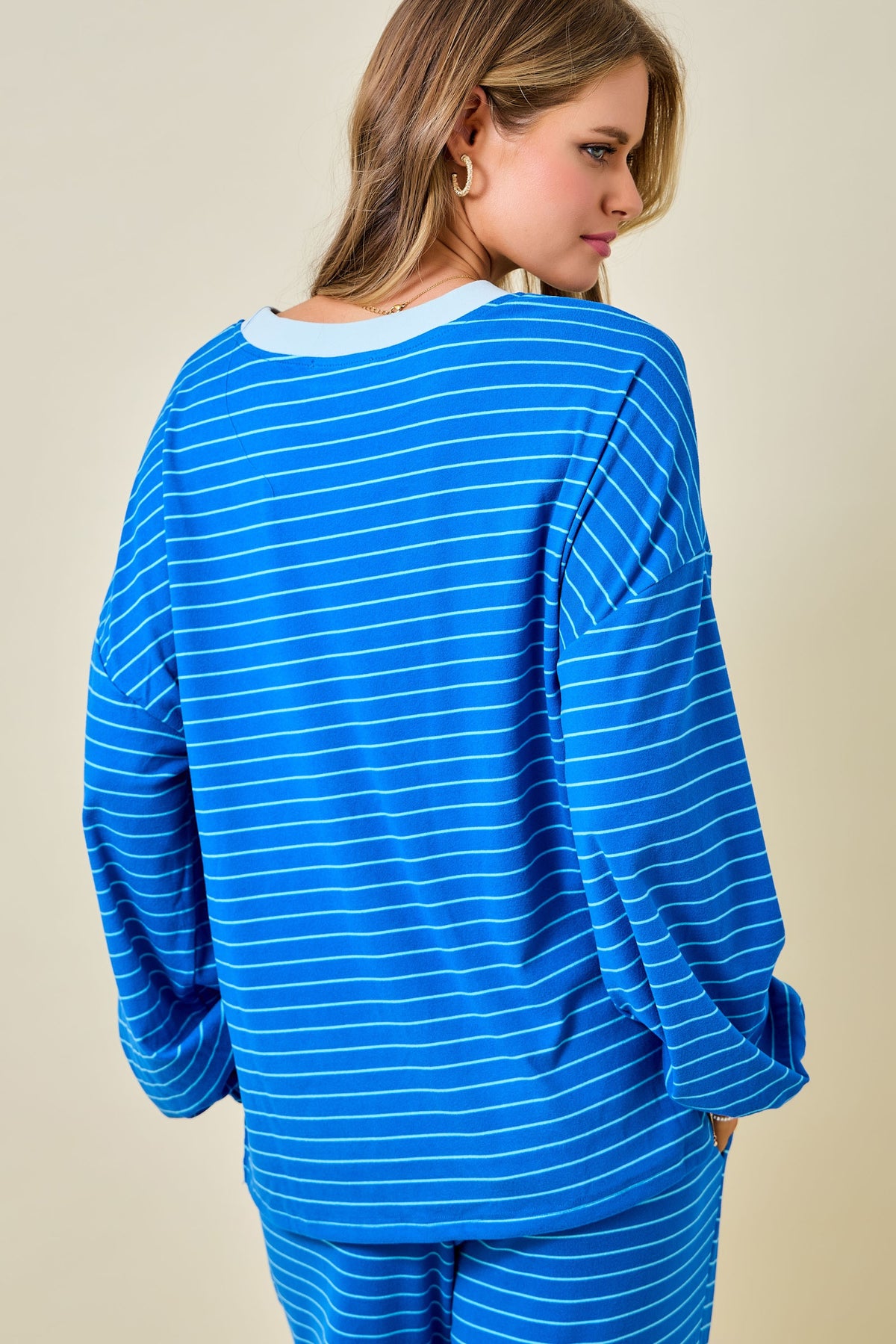 A woman wearing a bright blue and white striped long-sleeve top and matching pants, photographed from the back against a plain beige studio background.