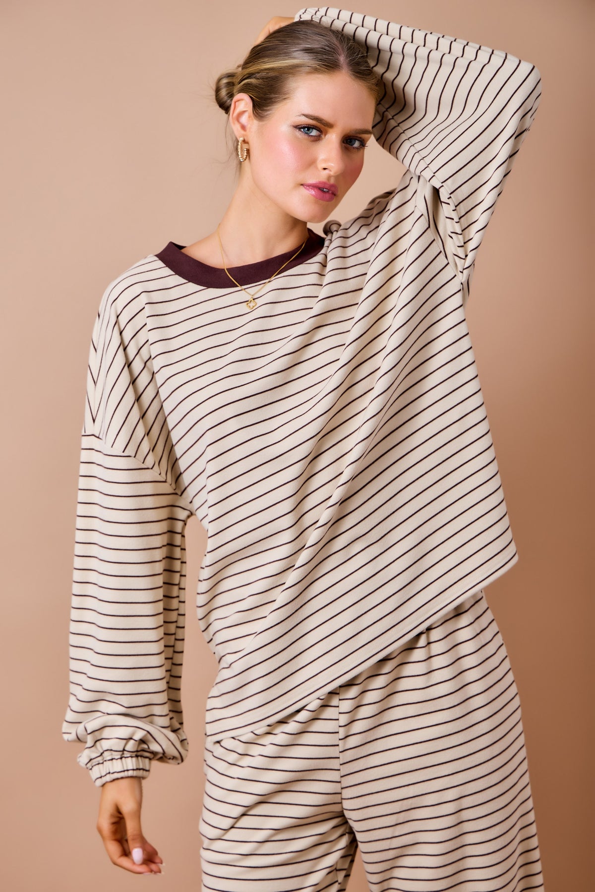 A woman modeling a matching two-piece loungewear set featuring a beige and dark brown striped long-sleeve top and pants, with a solid dark brown crew neck.