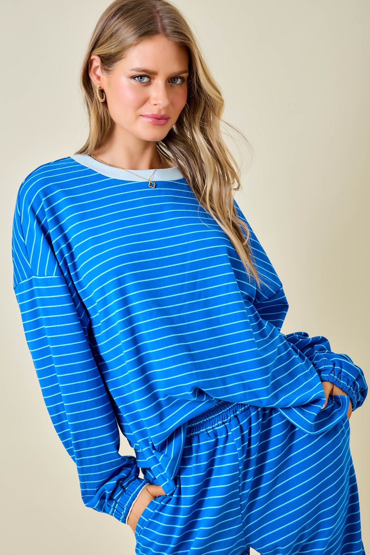A woman wearing a blue and white striped lounge set with a long-sleeve top and matching pants, posed against a solid beige background.