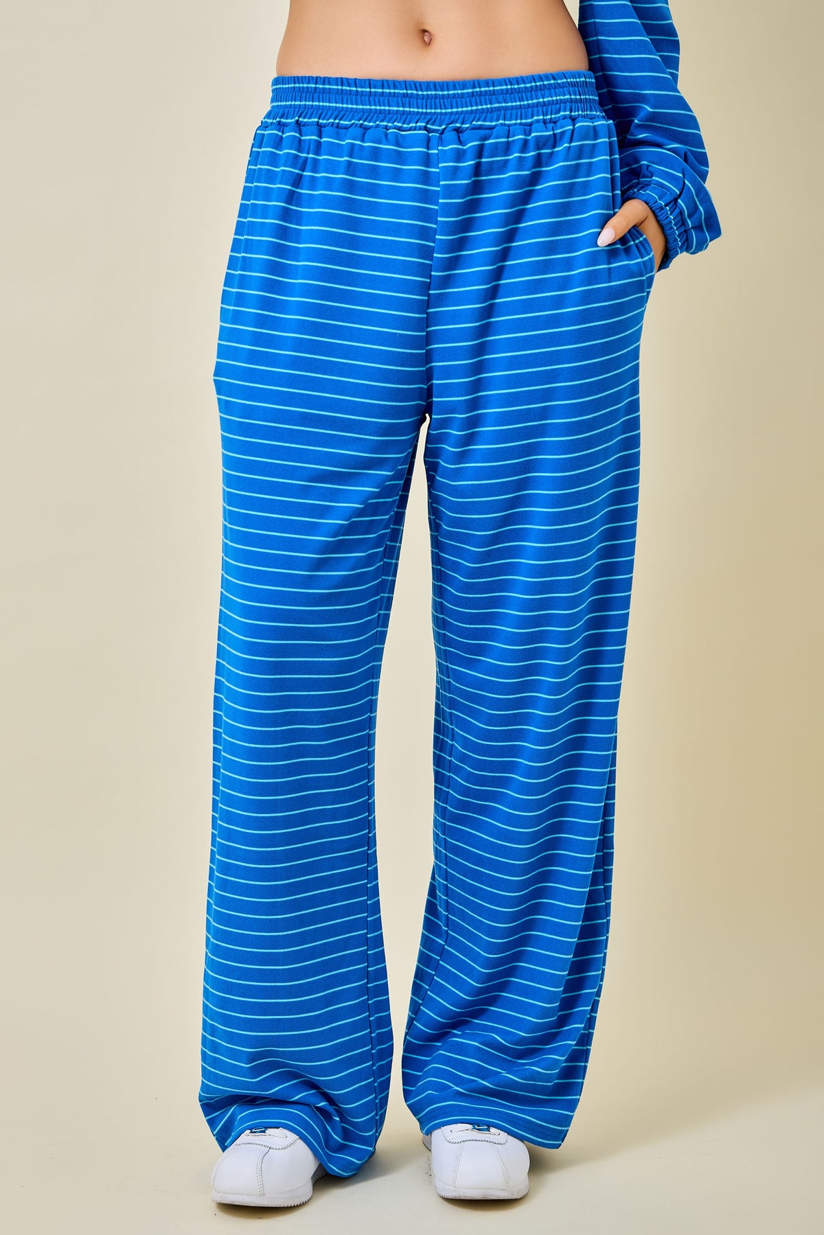 A person wearing bright blue wide-leg pants with thin white horizontal stripes, shown from the waist down against a plain beige studio background.