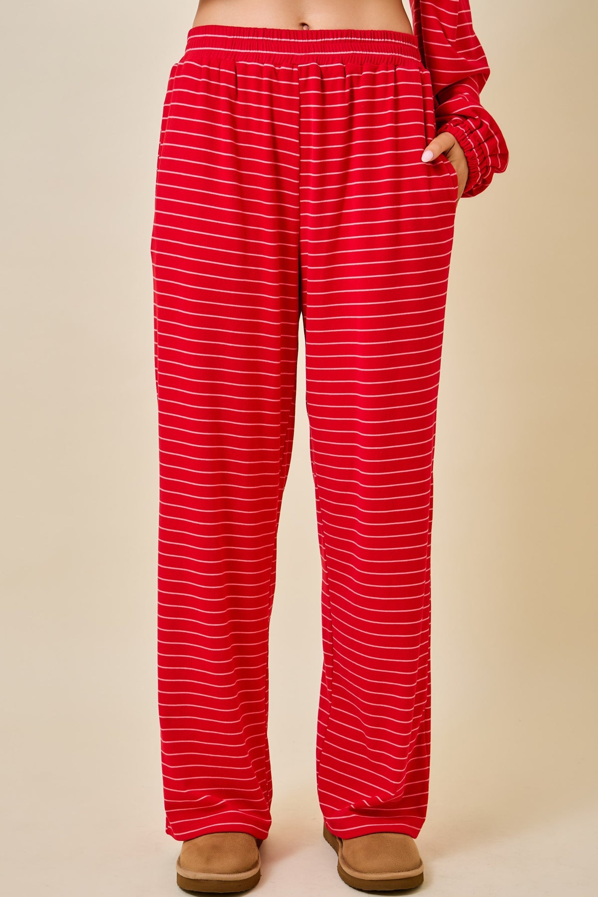 Red and white striped lounge pants with an elastic waistband and side pockets, shown on a model from the waist down against a beige studio background.