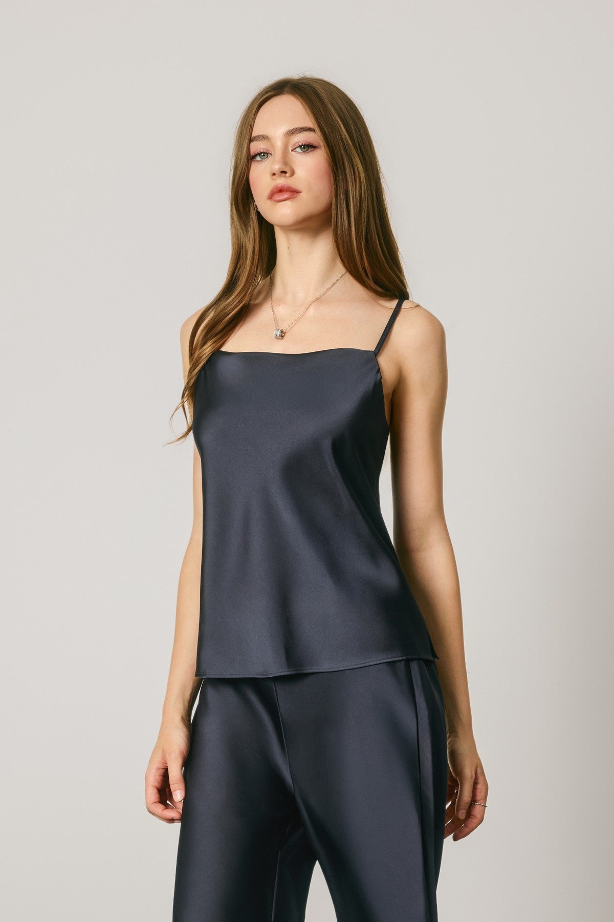A woman modeling a dark navy satin camisole top and matching satin pants against a light gray studio background.