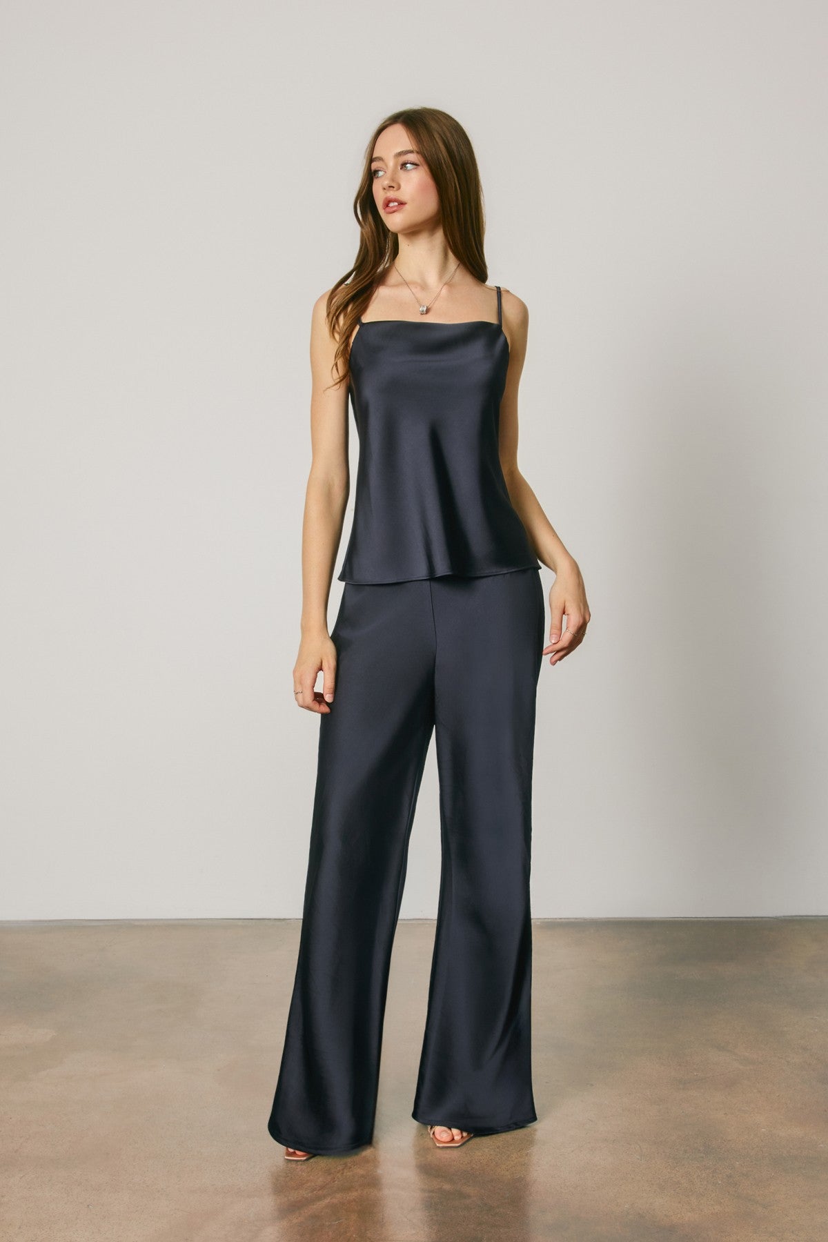 A woman modeling a matching dark navy satin camisole top and wide-leg pants set against a neutral studio backdrop.